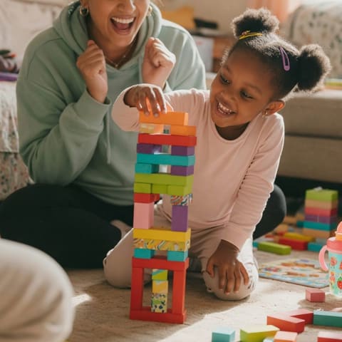 A parent cheering as a young child proudly builds a tall tower of colorful blocks