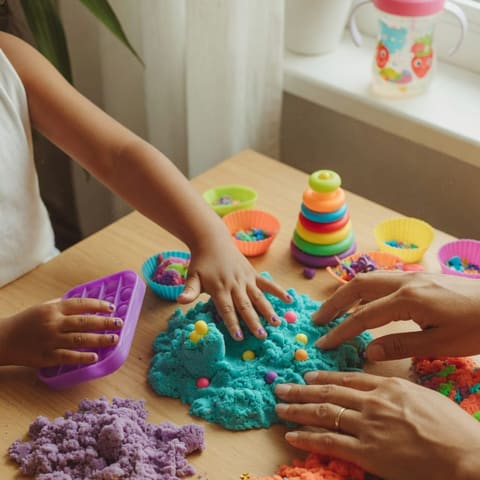 Close-up of a young child's hands and an adult's hands playing with colorful sensory toys and kinetic sand